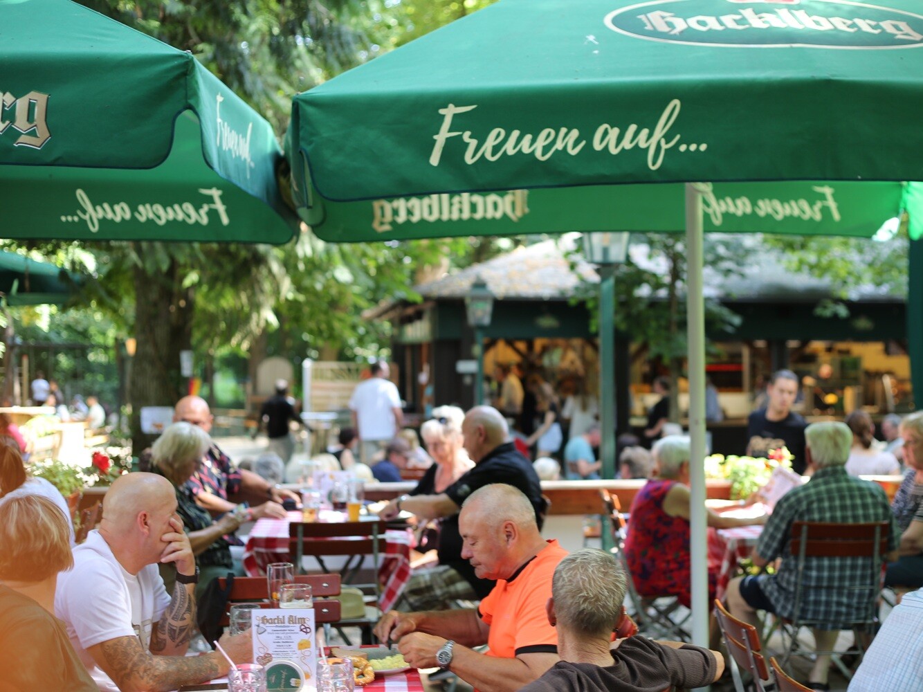 Eine Gruppe von Menschen sitzt an Tischen unter Sonnenschirmen.